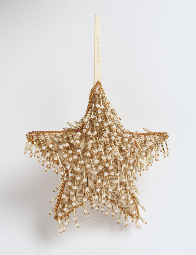 Beige fabric star ornament with gold beads and pearl-like embellishments hanging by a beige ribbon with text