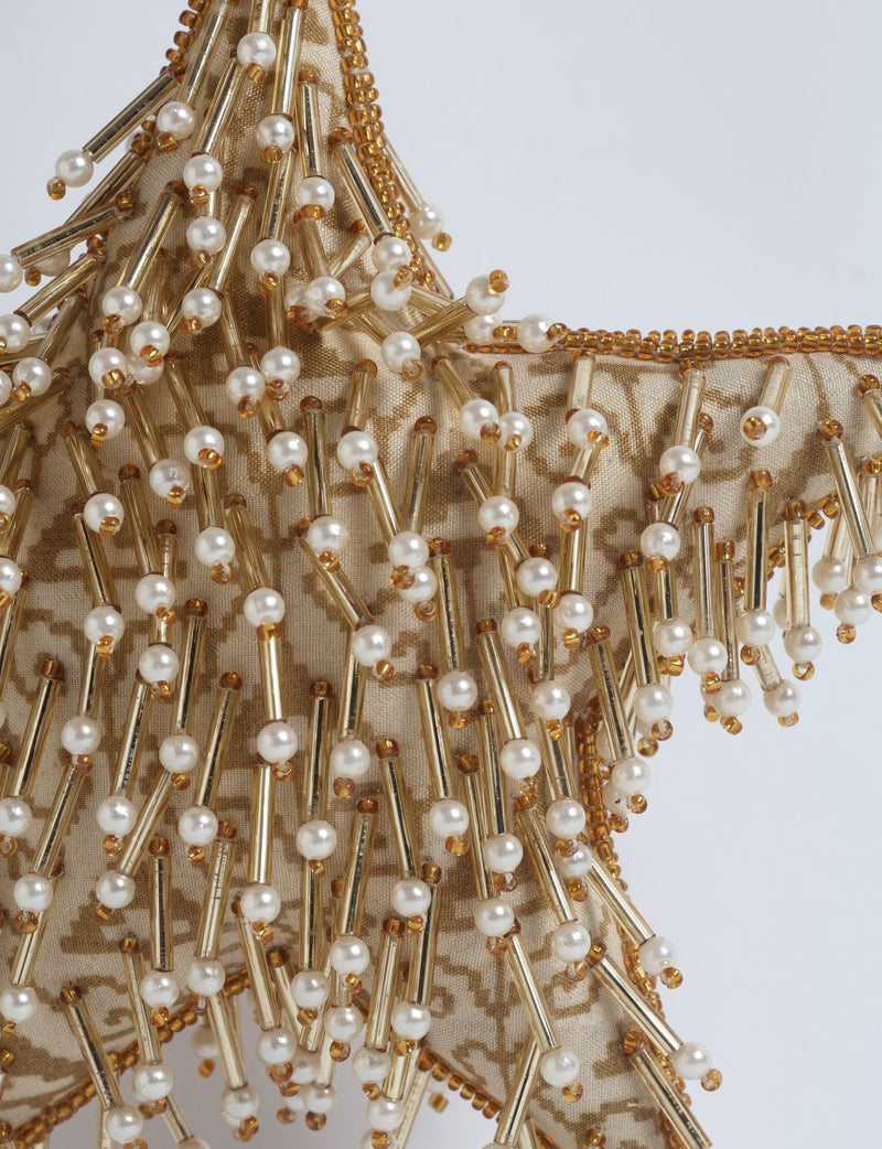 Beige fabric star ornament with gold beads and white pearl-like embellishments, close-up view on white background