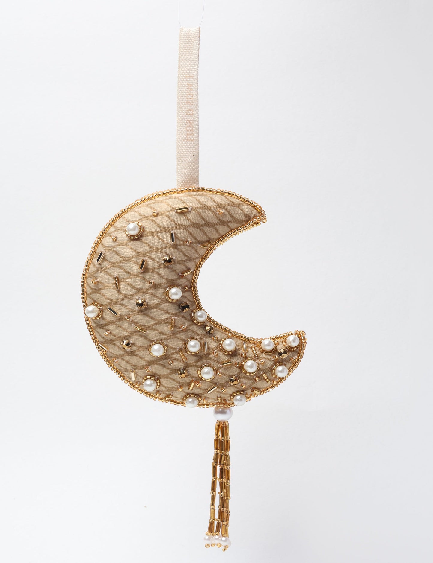 A crescent moon ornament made from ivory and cream recycled fabric, filled with organic cotton, embellished with gold stones and beads. This recycled clothing piece aligns with circular fashion, earth friendly clothing, and fashion revolution ideals, crafted to support repurposed clothing and eco friendly fashion.