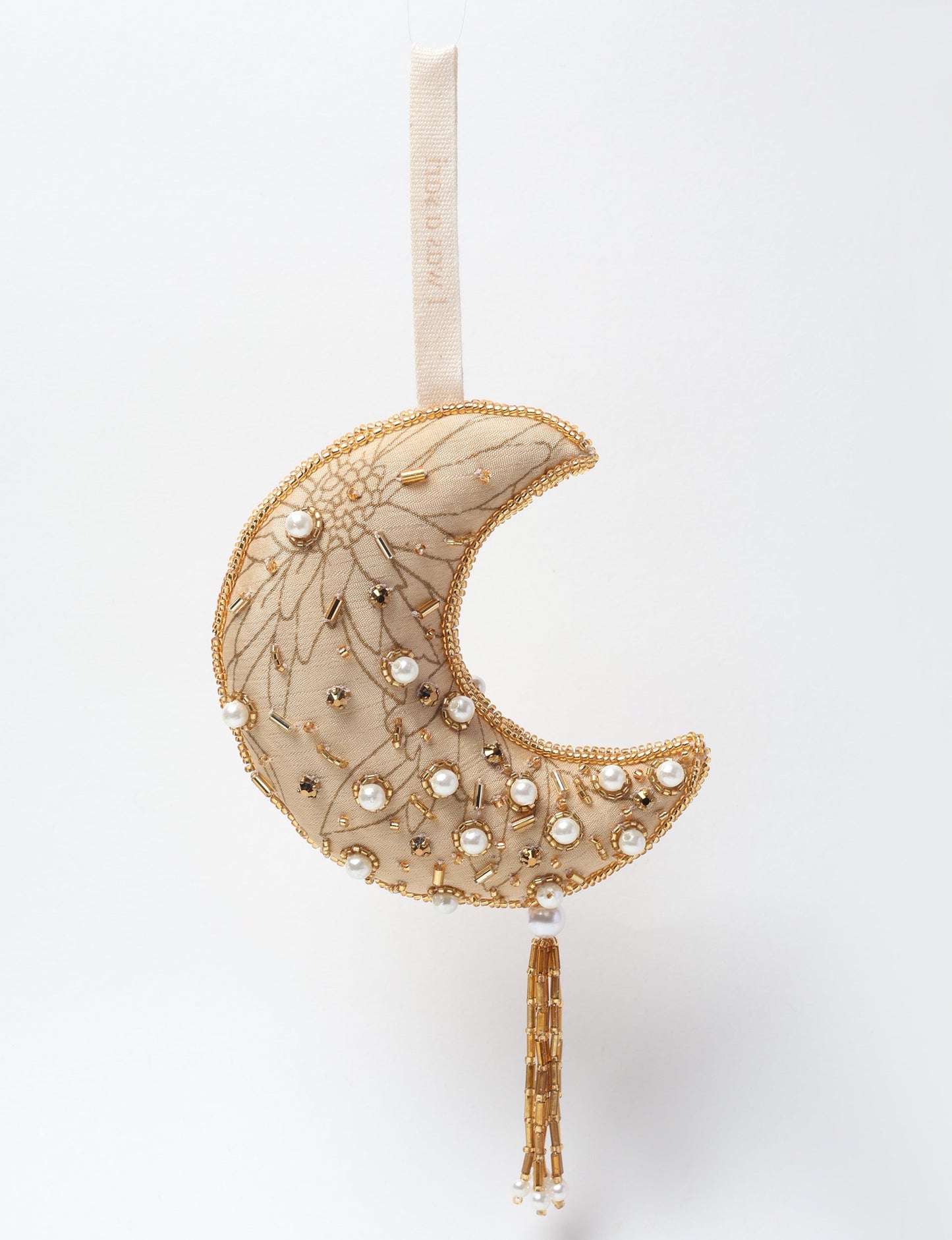 A crescent moon ornament made from ivory and cream recycled fabric, filled with organic cotton, embellished with gold stones and beads. This recycled clothing piece aligns with circular fashion, earth friendly clothing, and fashion revolution ideals, crafted to support repurposed clothing and eco friendly fashion.
