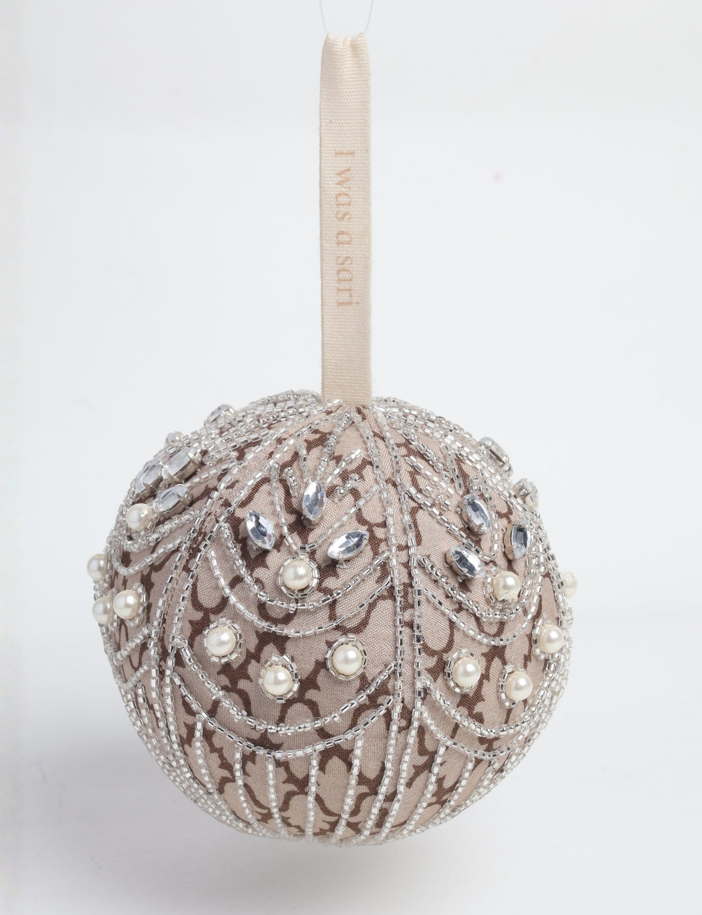 Silver colored ball ornament handcrafted from recycled sari fabric with silver embroidery and beads, representing upcycled clothing, sustainable women’s clothing, green fashion, slow fashion, and eco friendly fashion made from recycled materials.