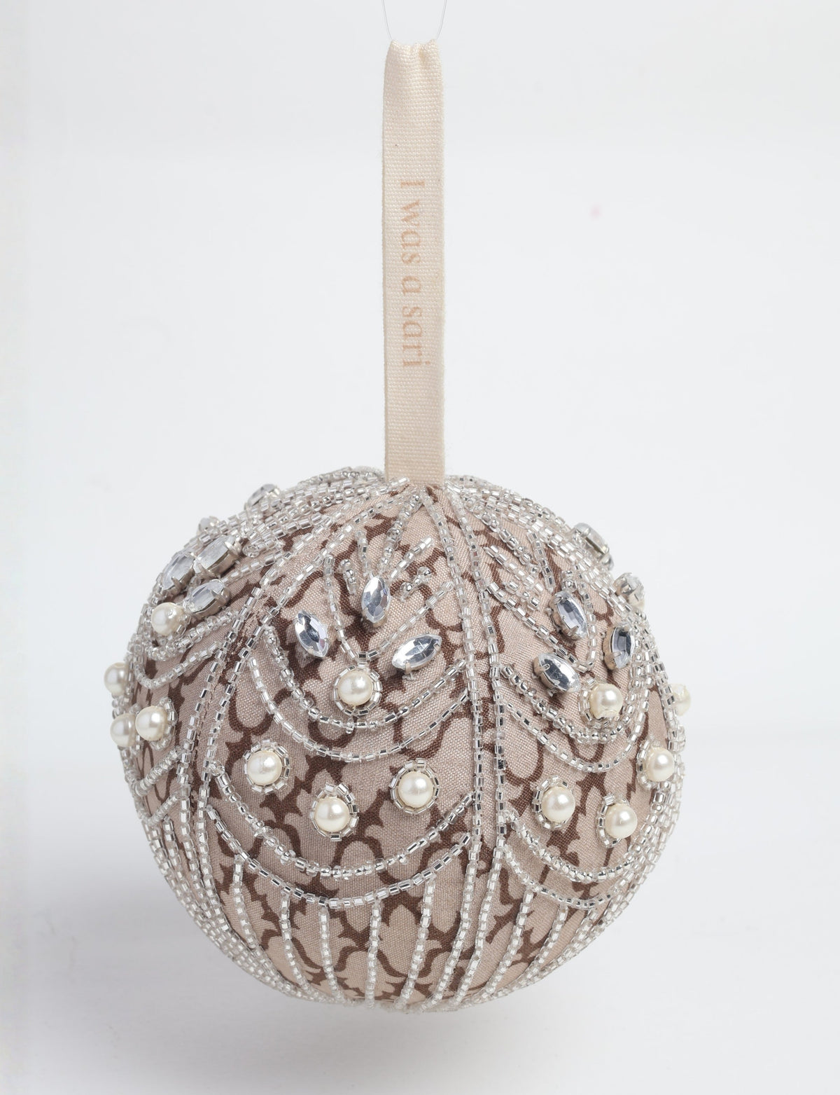 Silver fabric ball ornament with intricate beadwork, pearls, and clear gem embellishments, hanging by a beige loop with text