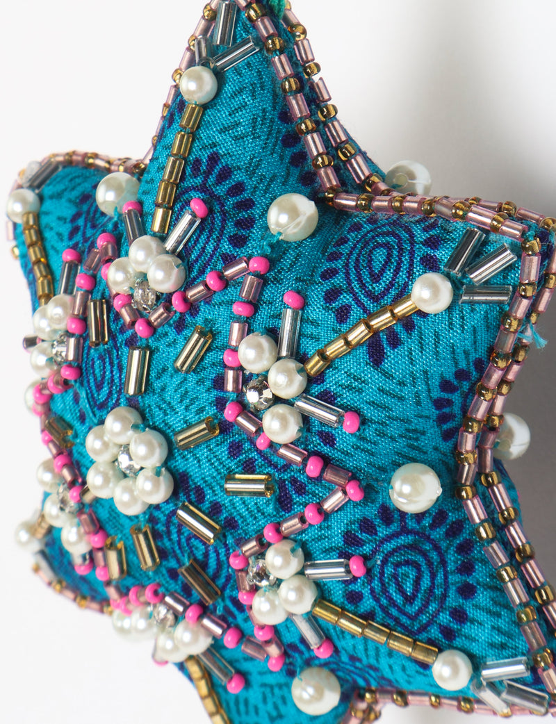 Teal fabric star-shaped snowflake ornament with bead and pearl embellishments, hanging by a teal fabric loop