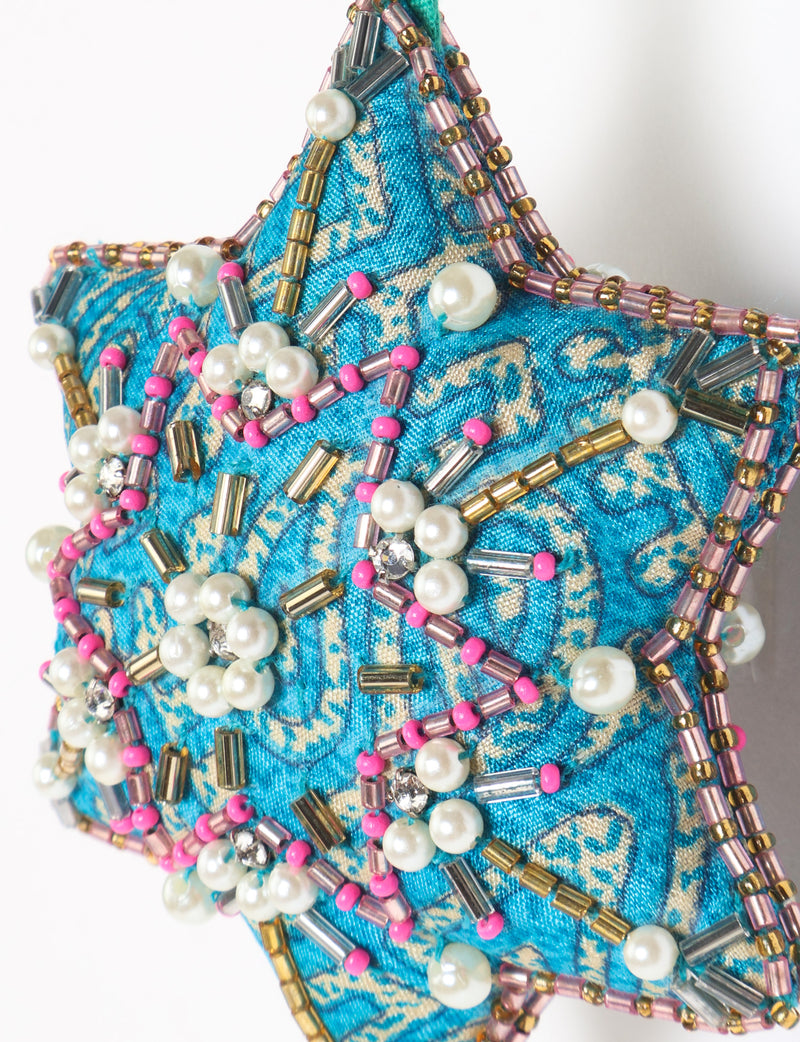 Teal fabric star-shaped snowflake ornament with bead and pearl embellishments, hanging by a teal fabric loop