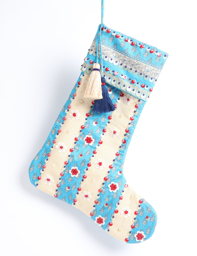 Blue and cream Christmas stocking with floral patterns, sequins, and two hanging tassels, shown hanging against white background