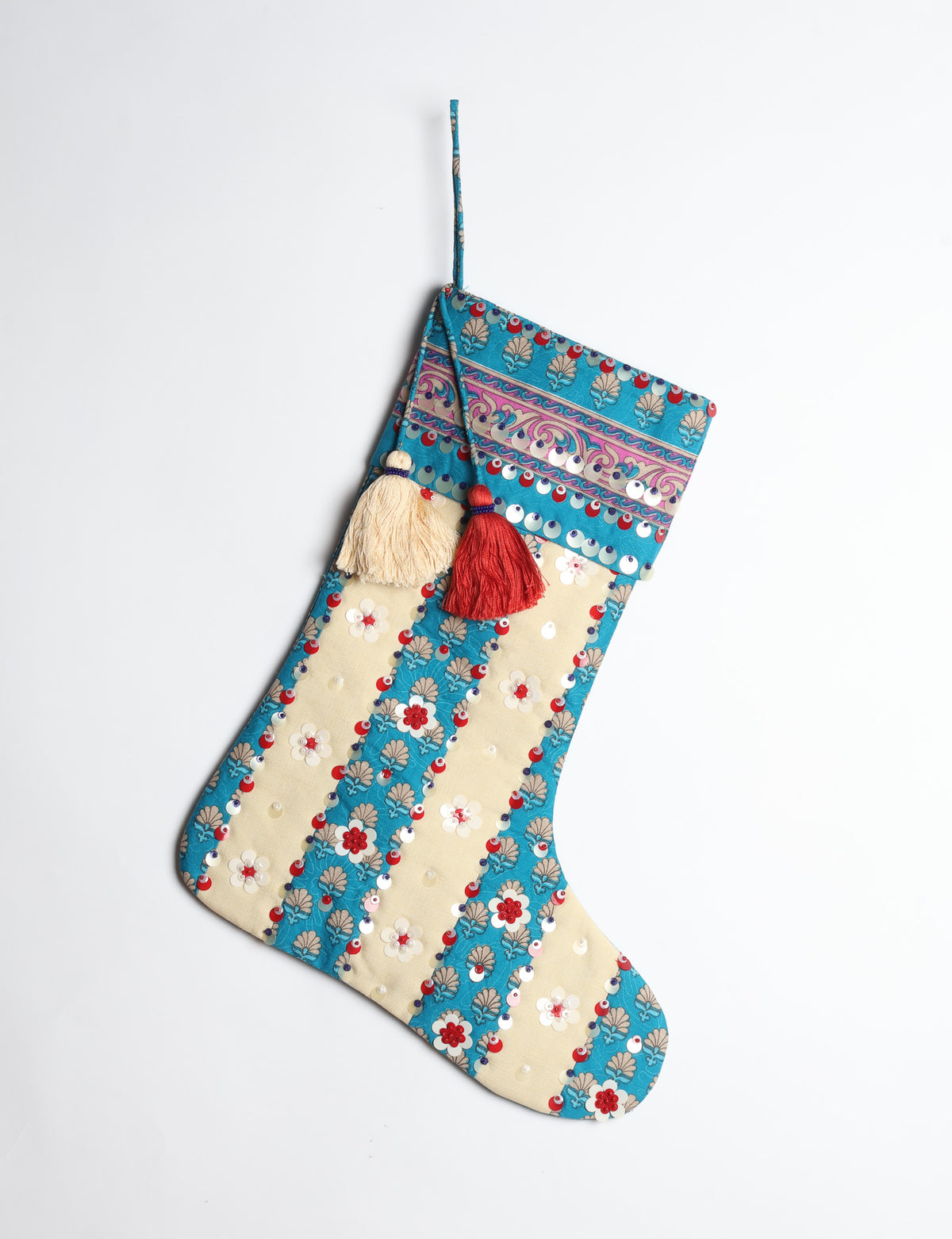 Blue and cream Christmas stocking with floral patterns, sequins, and two hanging tassels, shown hanging against white background