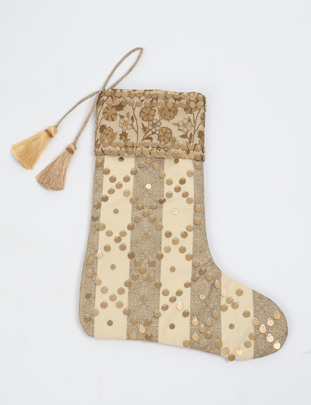 Beige and tan striped Christmas stocking with floral pattern, gold sequins, and two tassels on hanging loop, flat lay view