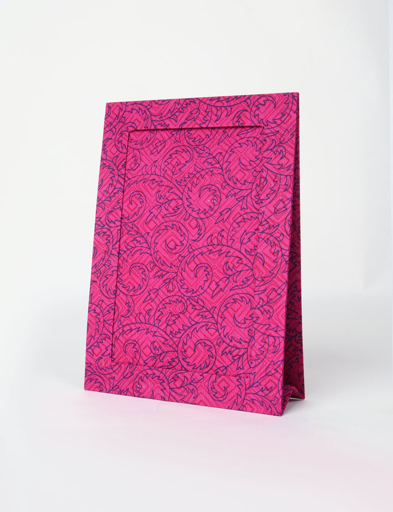 Pink photo frame with dark blue tropical leaf pattern, standing upright on a white surface, front angled view