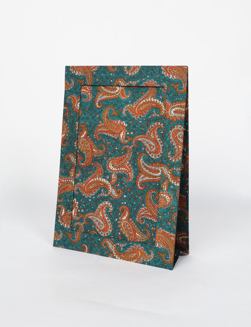 Folded fabric with teal background and orange paisley floral pattern, shown against a white backdrop