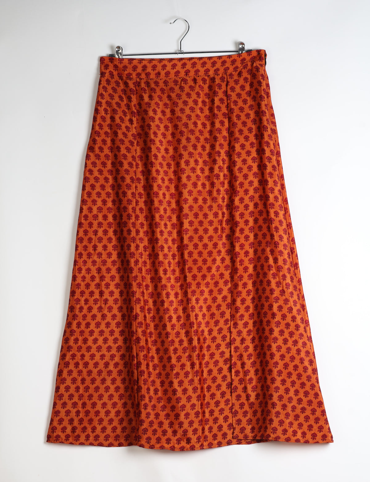 Orange A-line skirt with red micro floral pattern, front slit, hanging on metal hanger against white background