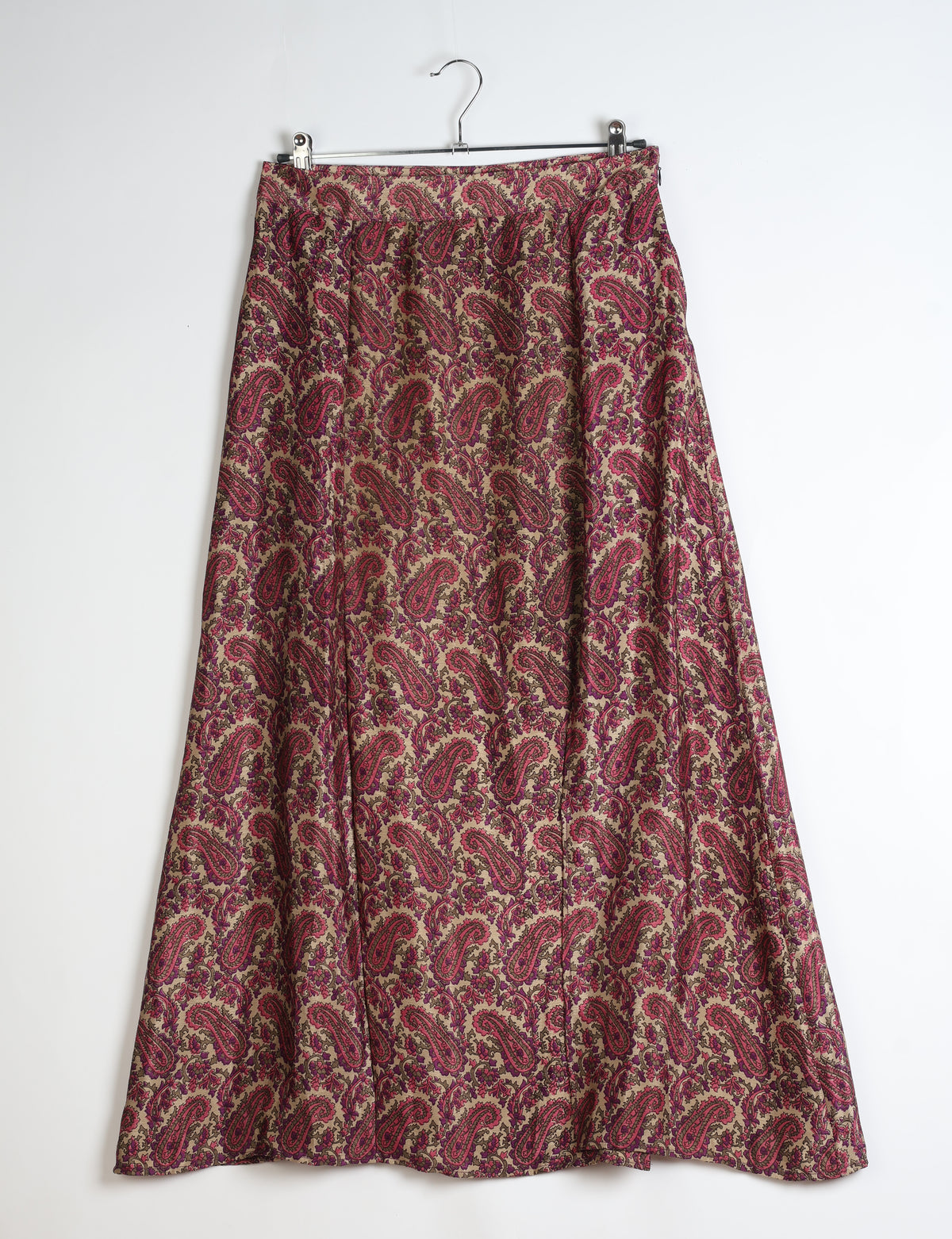 Pink paisley patterned A-line skirt with side slit hanging on a metal hanger against white background