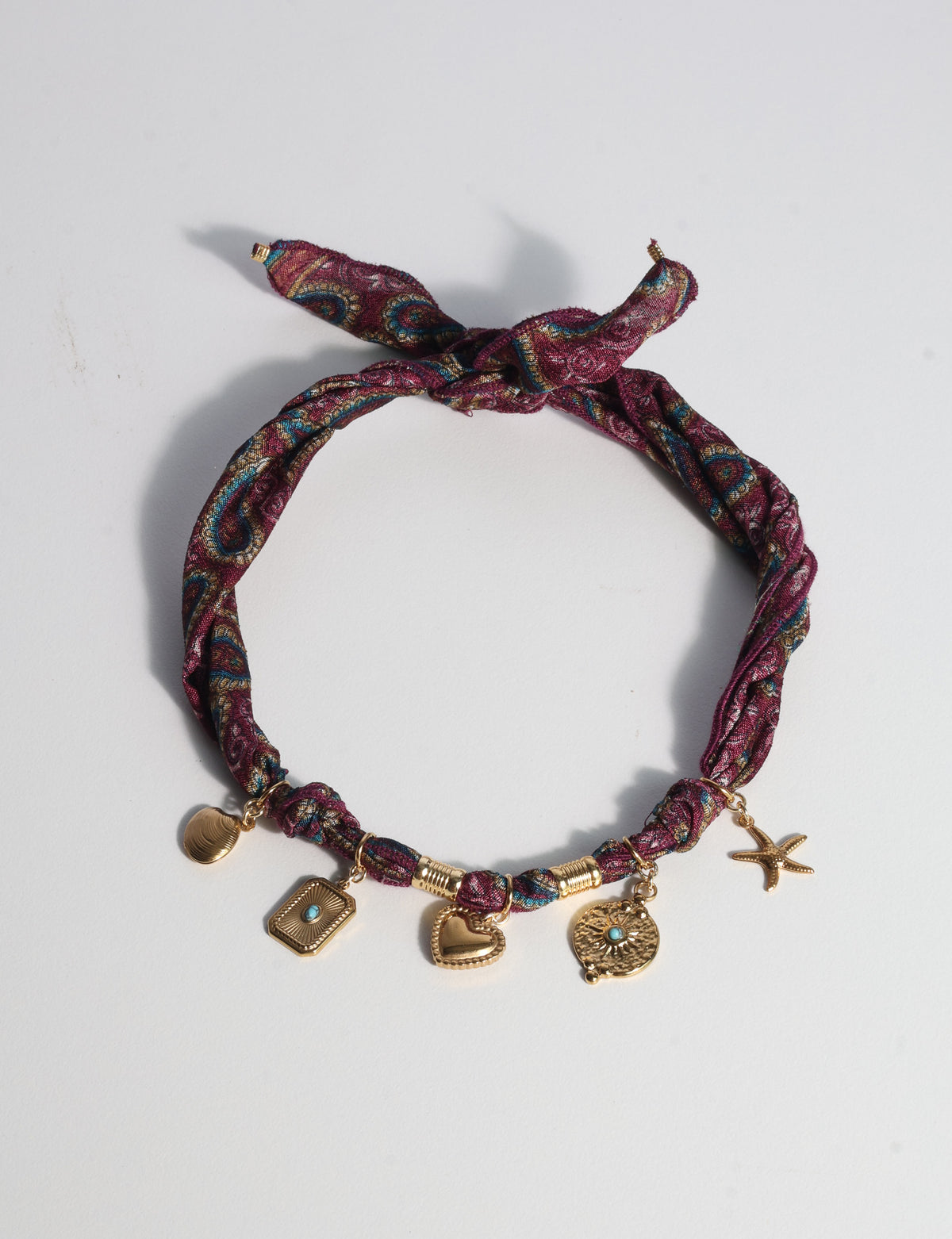 Red tropical patterned bandana necklace with gold-tone charms including a heart, starfish, and turquoise accents, flat lay view