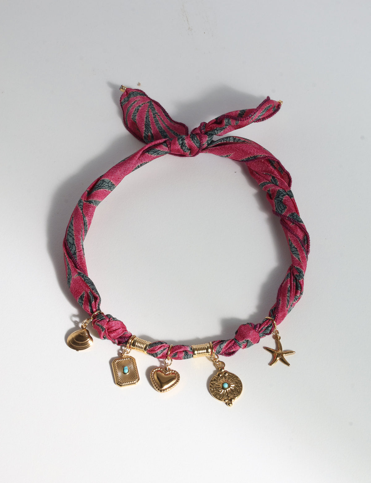 Pink abstract patterned bandana necklace with gold-tone charms including a heart, starfish, and shell, flat lay view