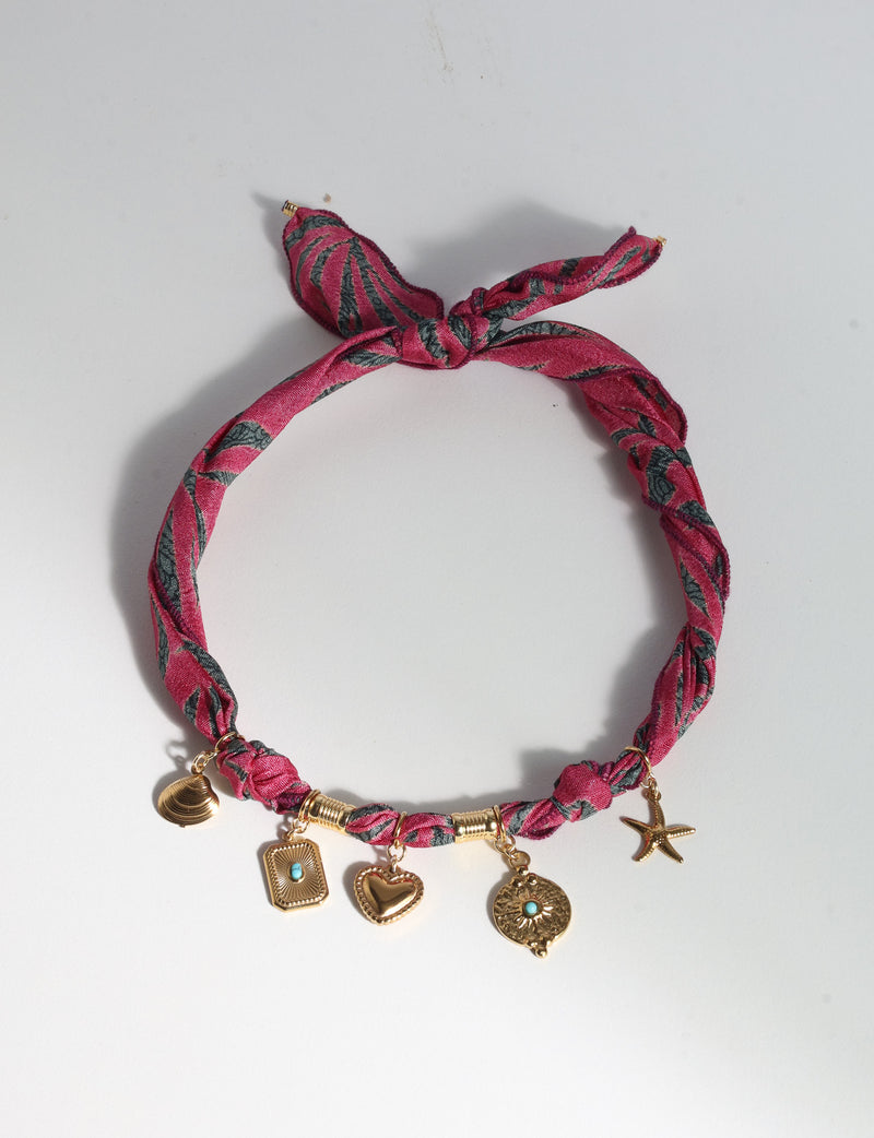 Pink abstract patterned bandana necklace with gold-tone charms including a heart, starfish, and shell, flat lay view