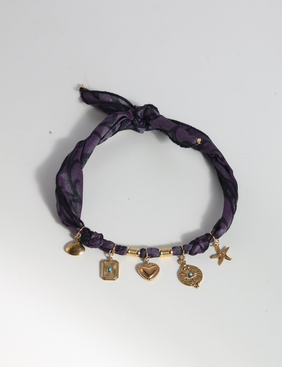 Purple abstract patterned bandana necklace with gold-tone charms including heart, starfish, and turquoise accents, flat lay view