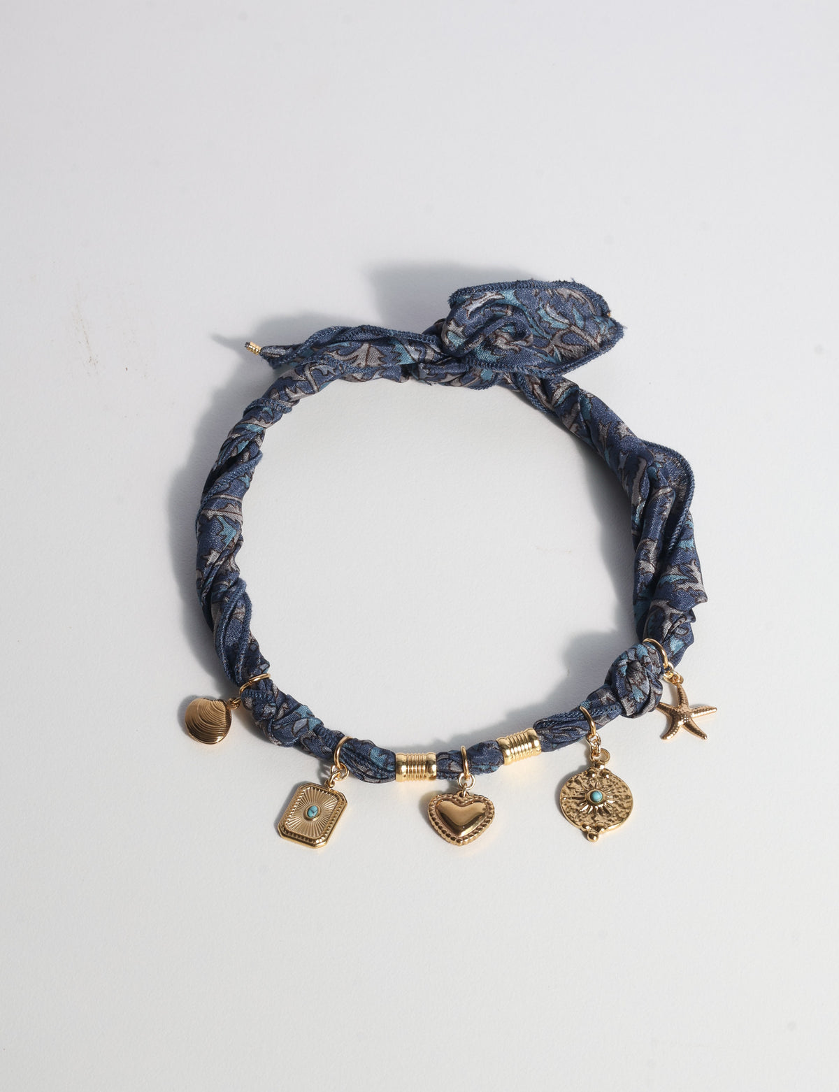Grey tropical patterned bandana necklace with gold-tone charms including heart, starfish, and shell, flat lay on white background