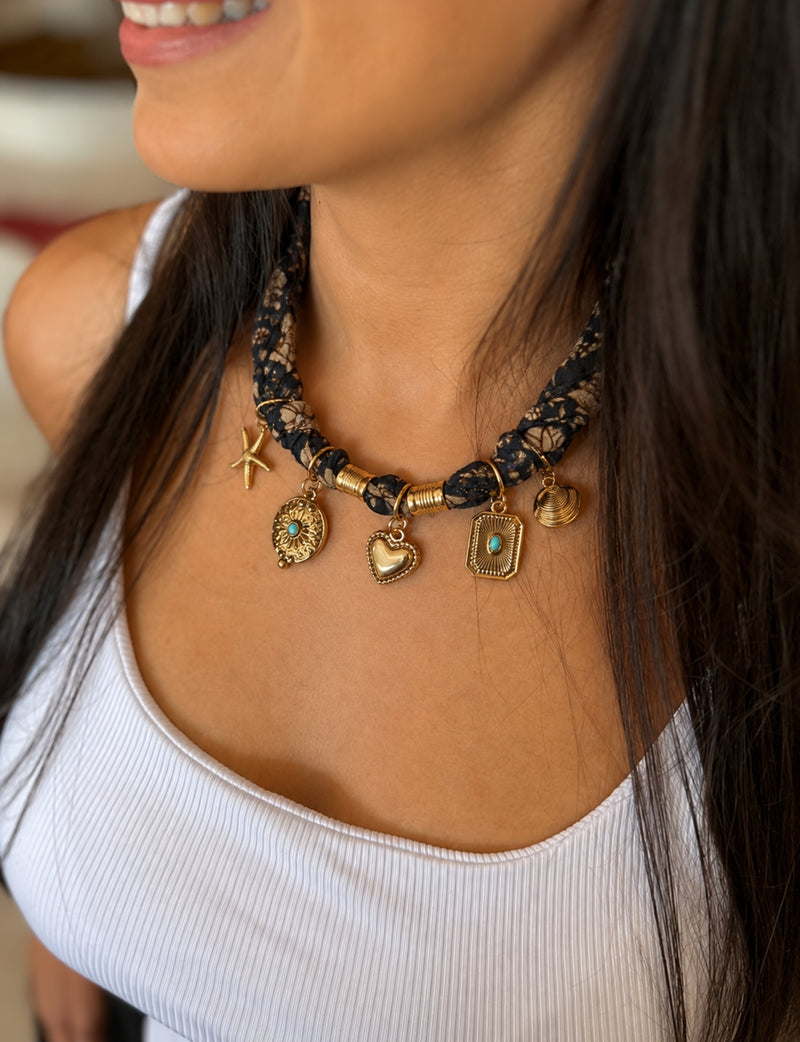 Black tropical patterned bandana necklace worn by model with gold charms including starfish, heart, and turquoise accents