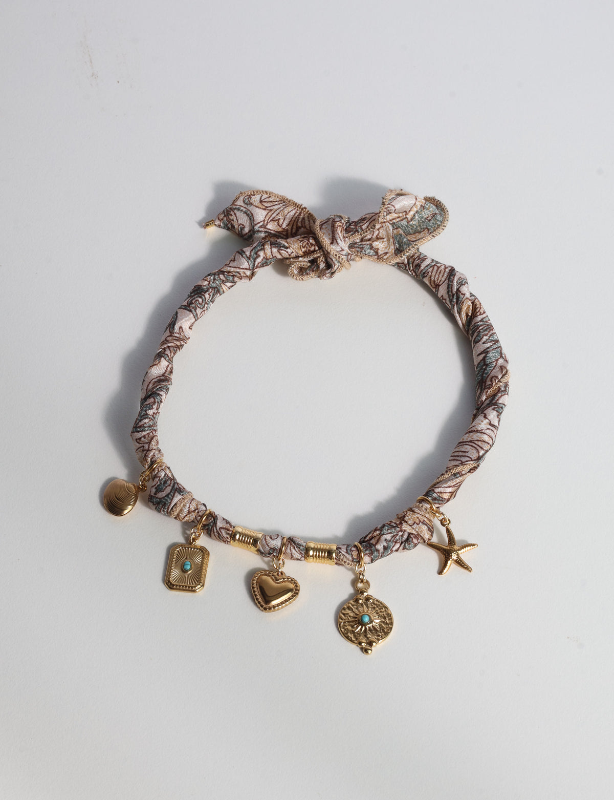 Beige tropical patterned bandana necklace with gold-tone charms including heart, starfish, and turquoise accents, flat lay view