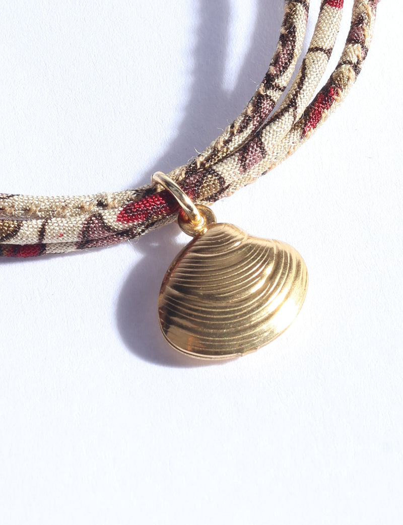 Beige cord bracelet with abstract brown and red pattern and gold-tone shell charm, close-up flat lay on white background