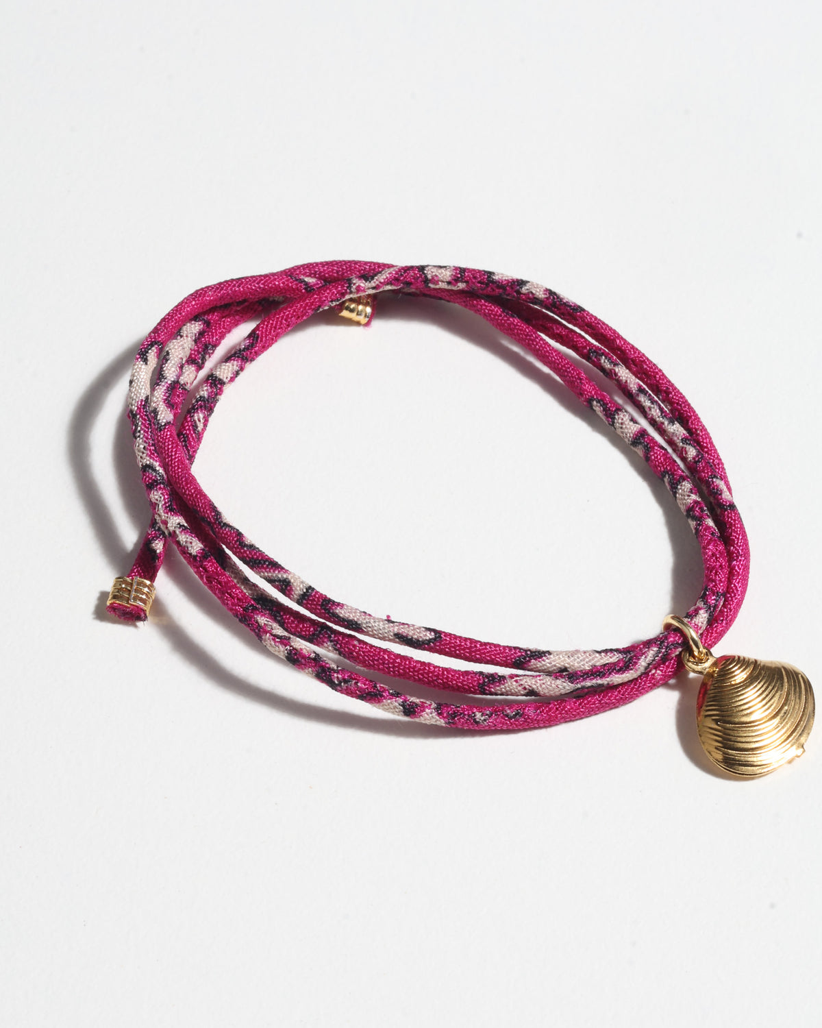 Pink floral patterned cord bracelet with a gold-tone shell charm, shown flat on a white background