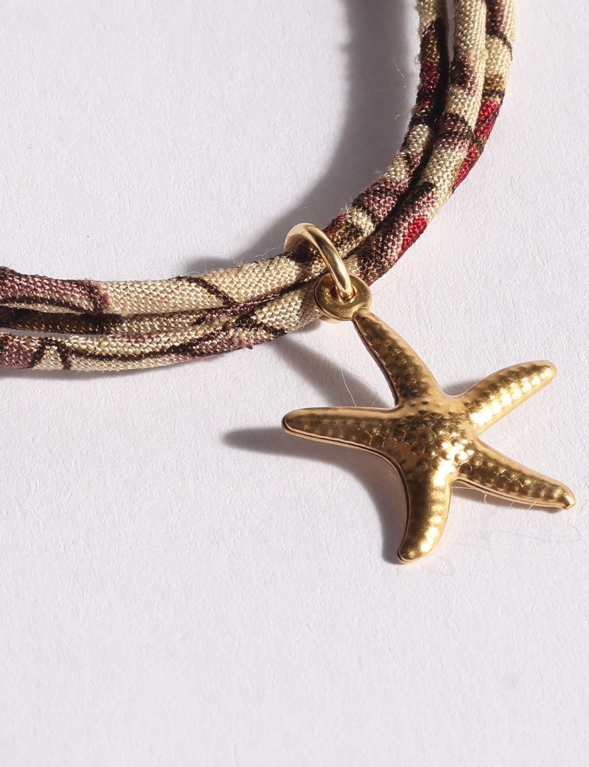 Brown and beige patterned cord bracelet with a gold-tone hammered starfish charm on a white background