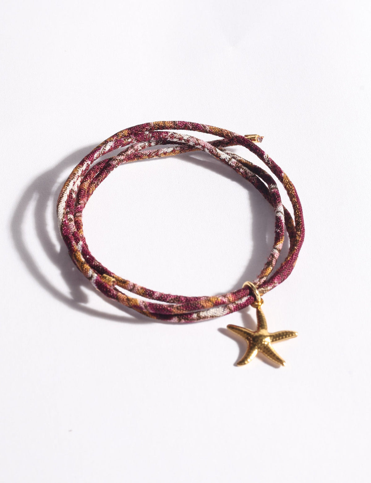 Multicolor cord bracelet with gold-tone starfish charm, shown coiled on white background, close-up front view