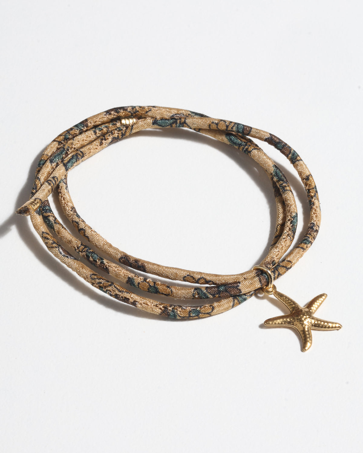 Beige tropical patterned cord bracelet with gold starfish charm, shown coiled on white background