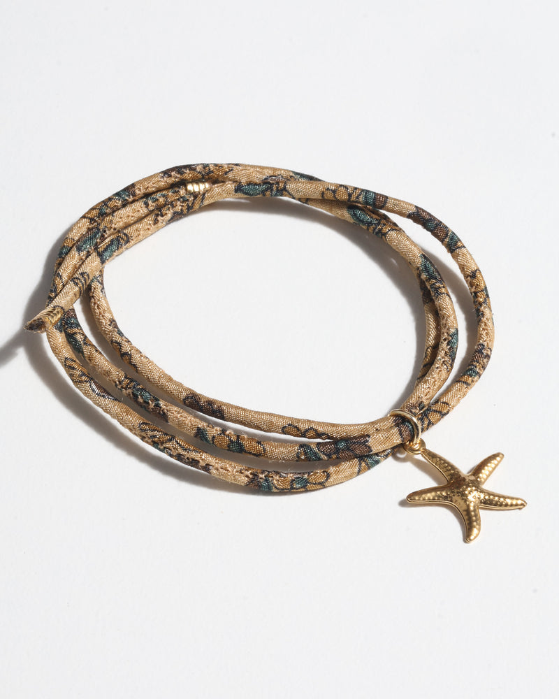 Beige tropical patterned cord bracelet with gold starfish charm, shown coiled on white background