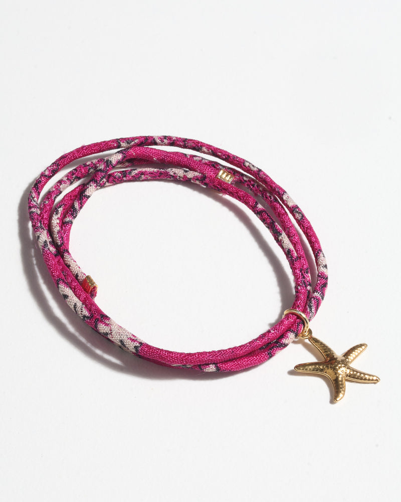Pink floral patterned cord bracelet wrapped with a gold starfish charm, shown flat on a white background