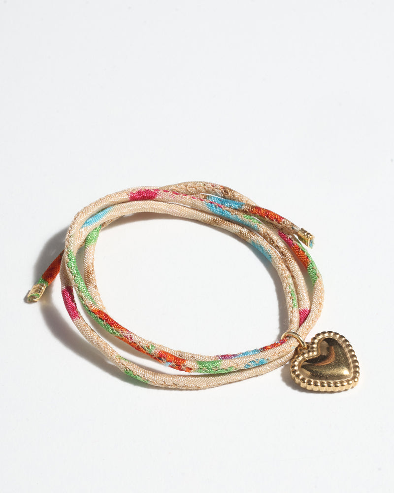Beige cord bracelet with multicolor abstract pattern and gold-tone heart charm, shown coiled on white background