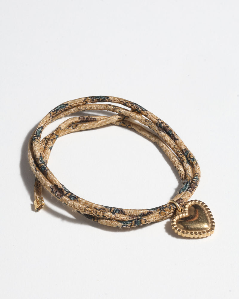 Beige tropical patterned cord bracelet with gold-tone heart charm and textured edges, shown flat on white background