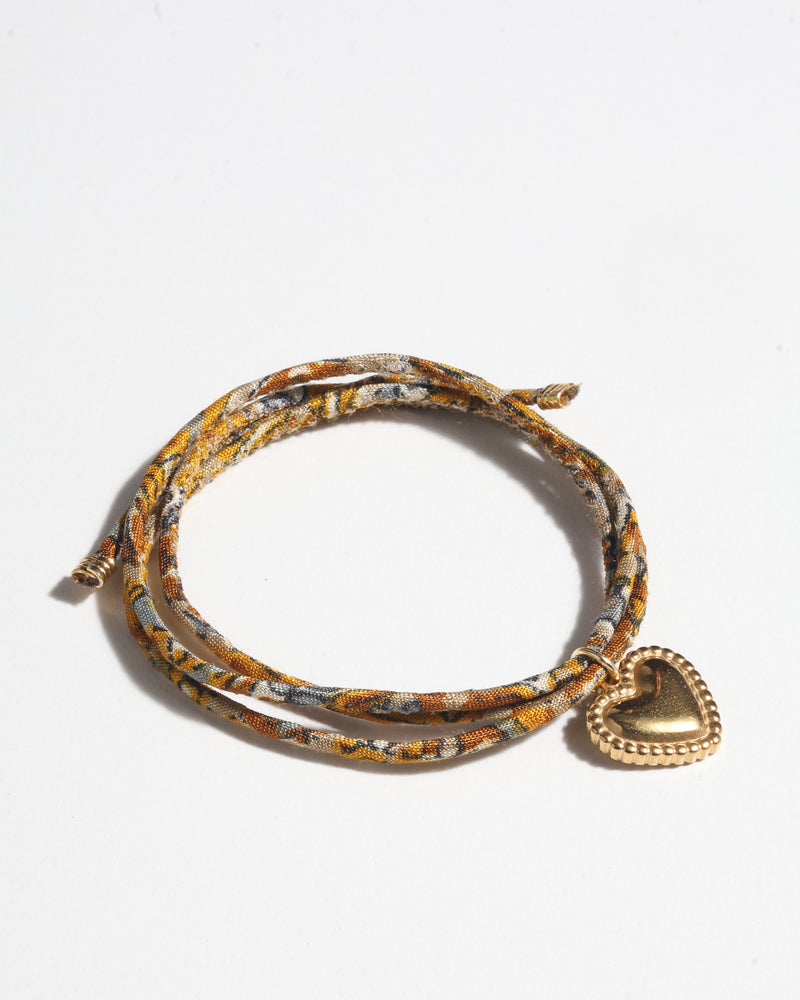 Yellow tropical patterned cord bracelet with gold-tone heart charm, shown flat on white background