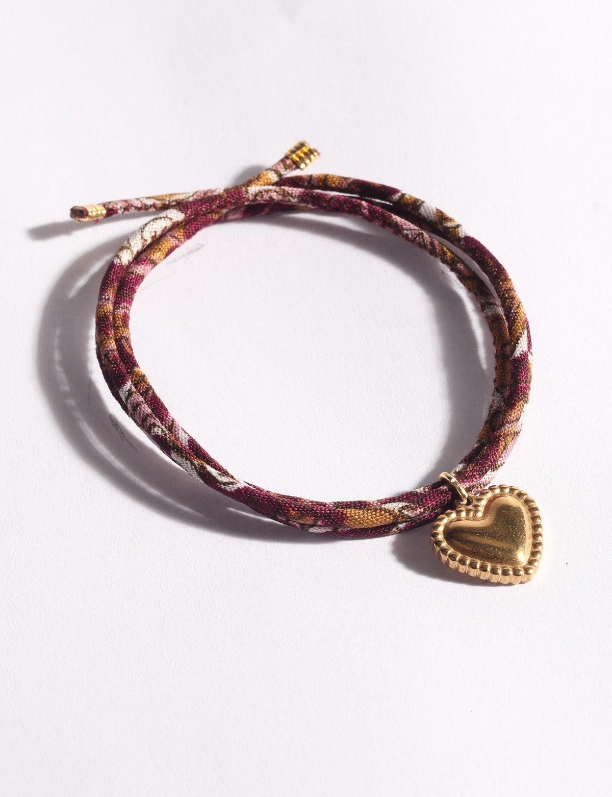 Red, pink, and brown patterned cord bracelet with a gold-tone heart charm, shown flat on a white background