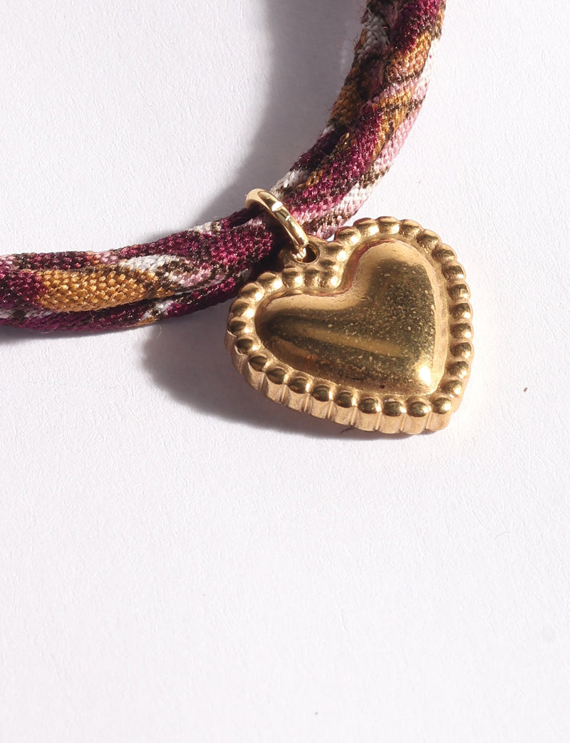 Red, pink, and gold abstract patterned cord bracelet with a gold heart-shaped charm in close-up view