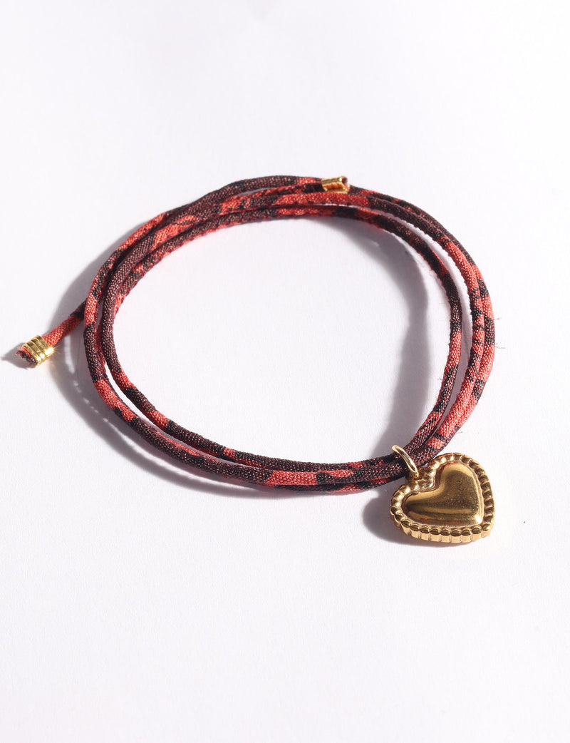 Brown and red abstract patterned cord bracelet with a gold-tone heart-shaped charm, shown flat on white background