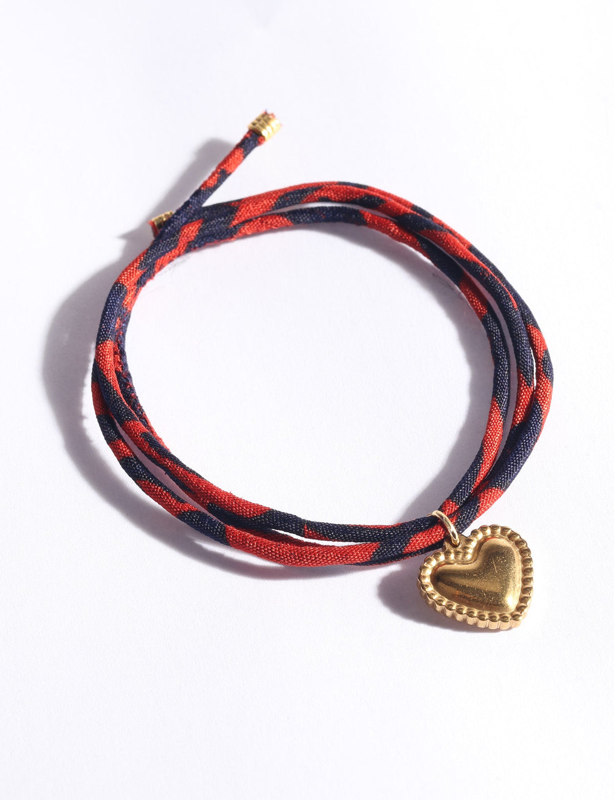 Red and navy abstract patterned cord bracelet with a gold heart-shaped charm, shown flat on a white background