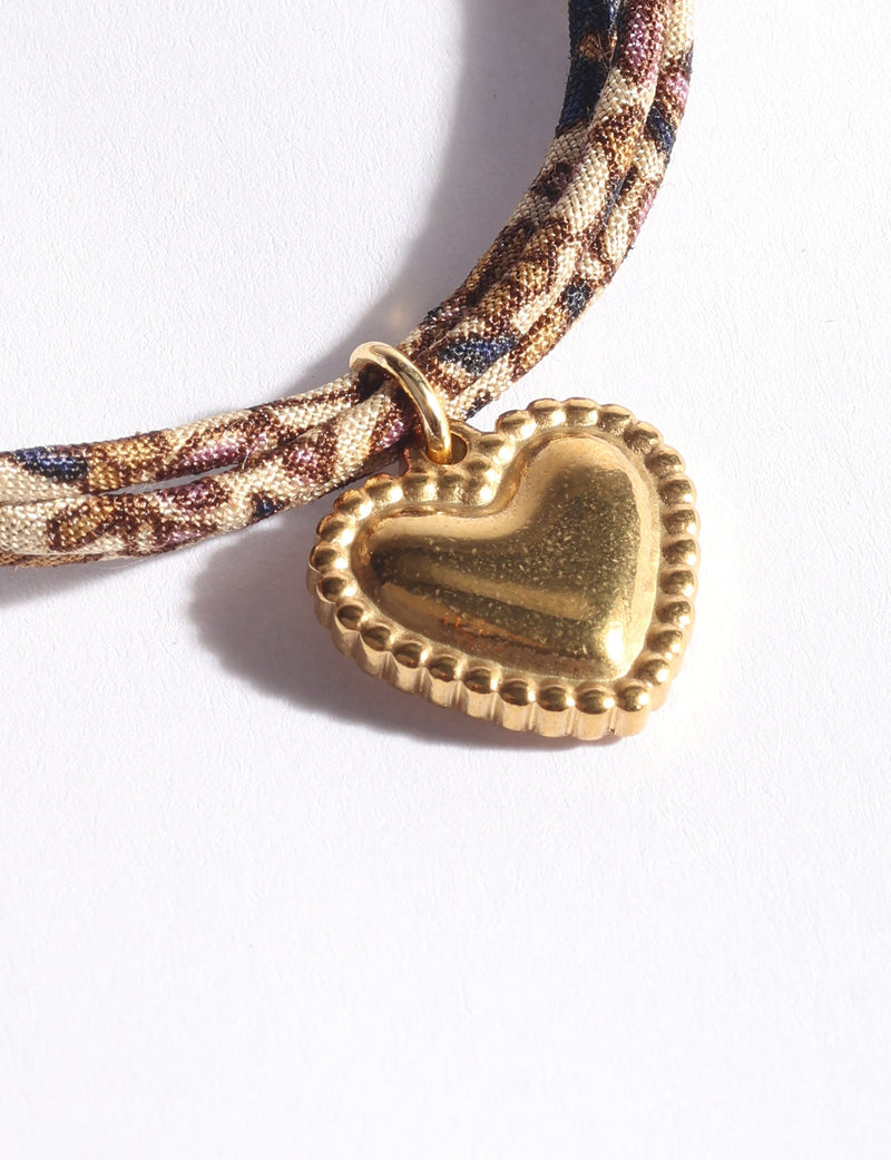 Beige abstract patterned cord bracelet with a gold-tone heart-shaped charm, close-up front view on white background