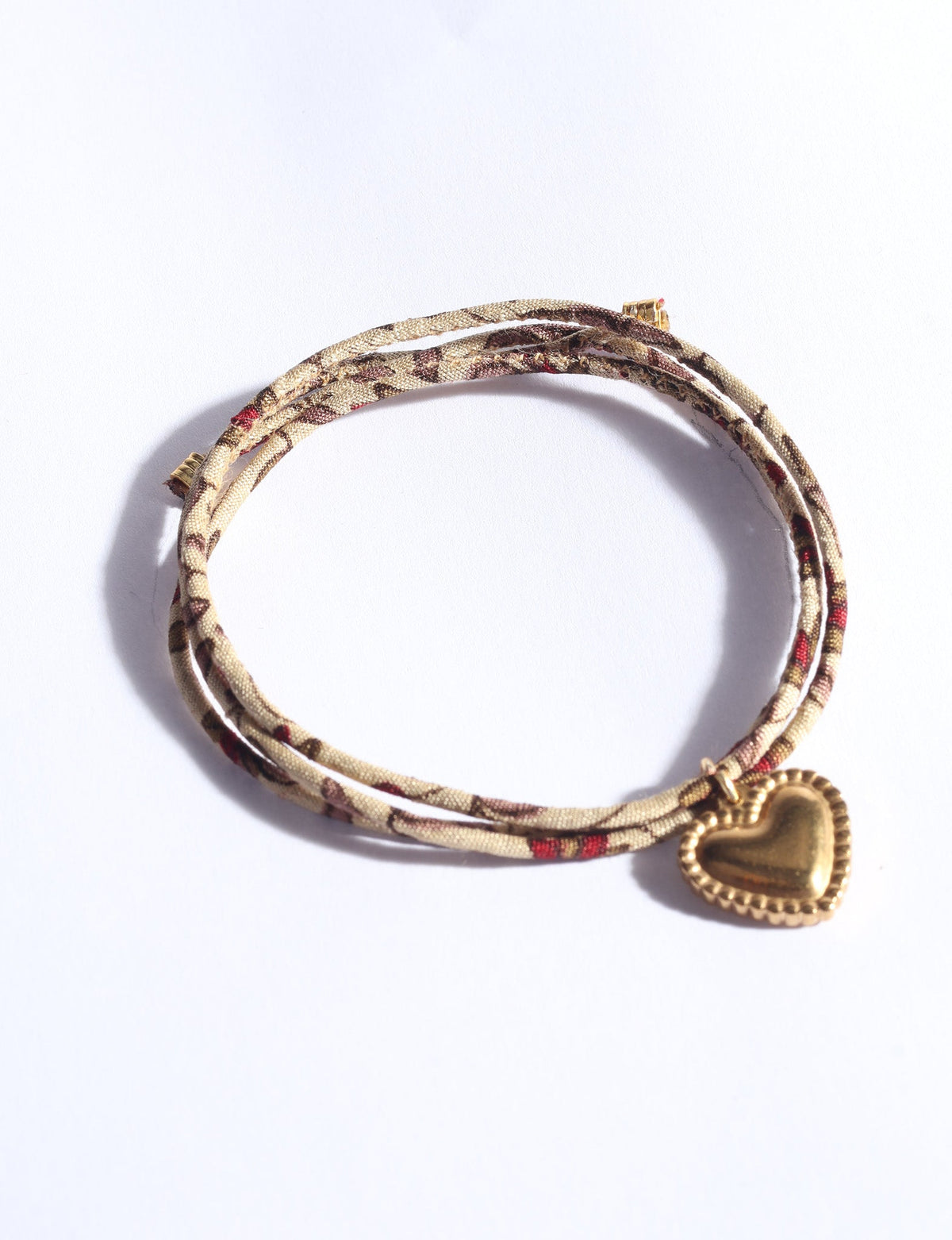 Beige cord bracelet with abstract brown and red pattern, featuring a gold heart-shaped charm, shown flat on white background