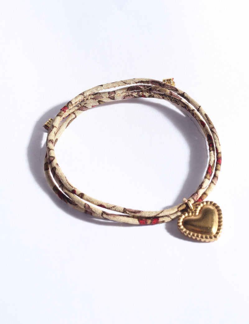Beige cord bracelet with abstract brown and red pattern, featuring a gold heart-shaped charm, shown flat on white background