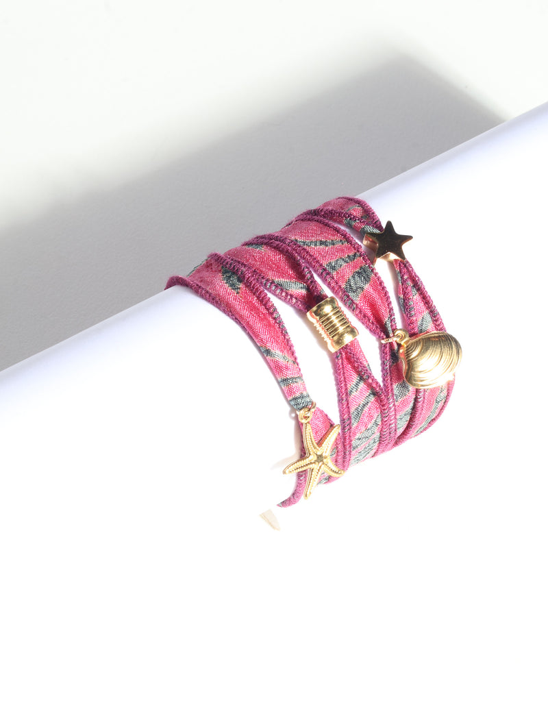 Pink and gray patterned wrap-around fabric bracelet with gold star, shell, and starfish charms, shown flat on white background