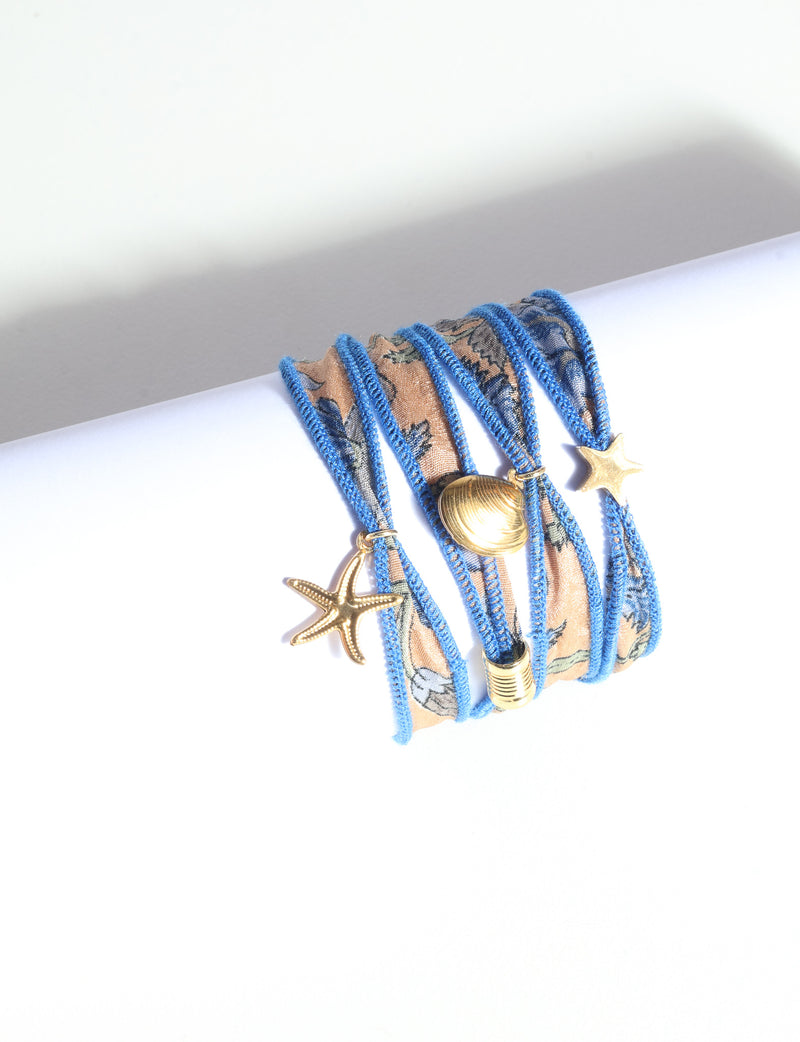 Wrap-around bracelet with blue-edged orange abstract fabric and gold-tone starfish, shell, and star charms on white background