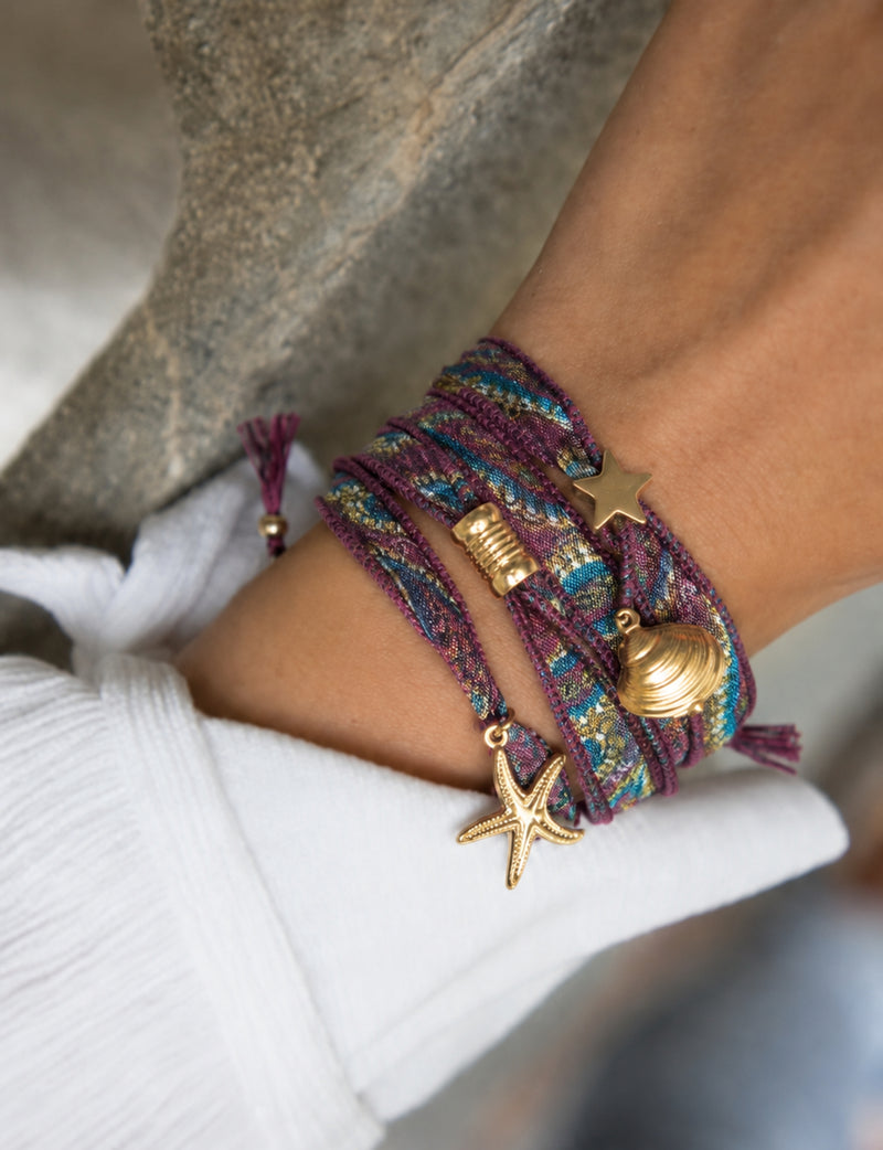 Wrap-around bracelet with purple, blue, and gold abstract fabric and gold star, shell, and starfish charms on wrist