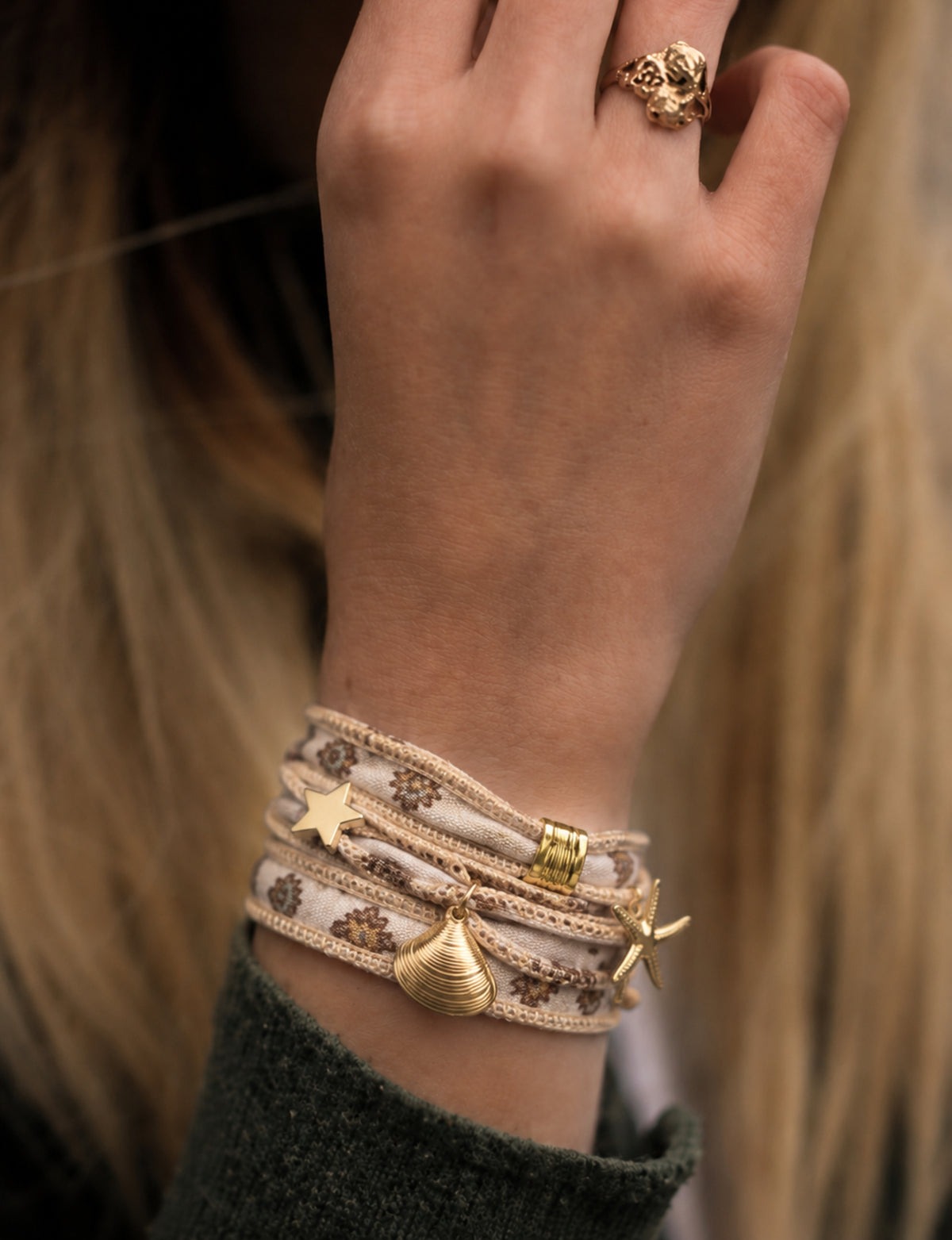 Beige wrap-around fabric bracelet with brown floral print and gold-tone star, shell, and starfish charms worn on wrist