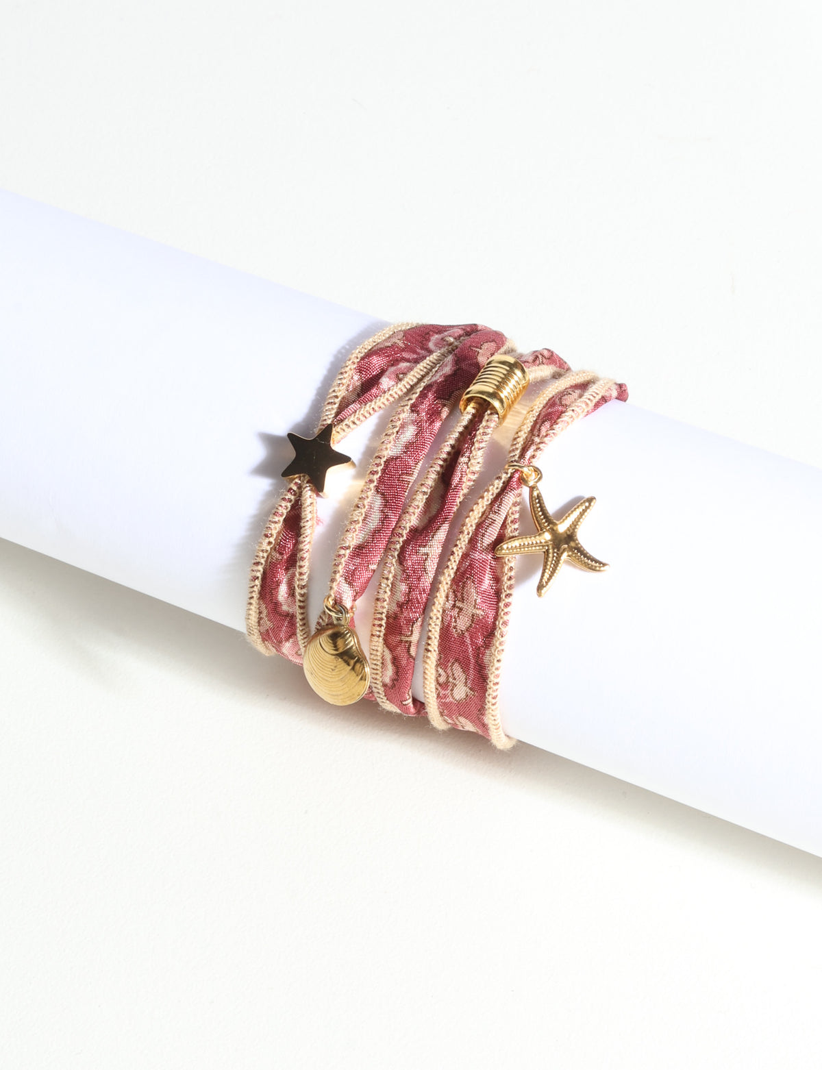 Wrap-around bracelet with orange abstract patterned fabric and gold-tone star, shell, and starfish charms on white display