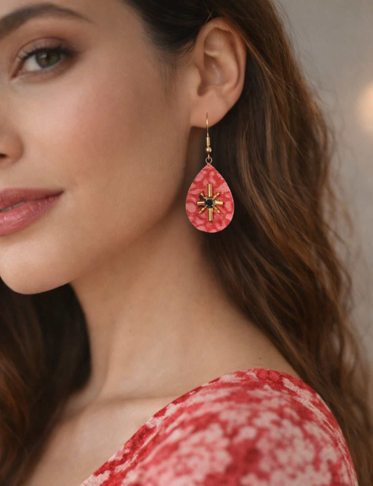 Woman wearing pink abstract teardrop earrings with gold and black bead embellishments, close-up side view