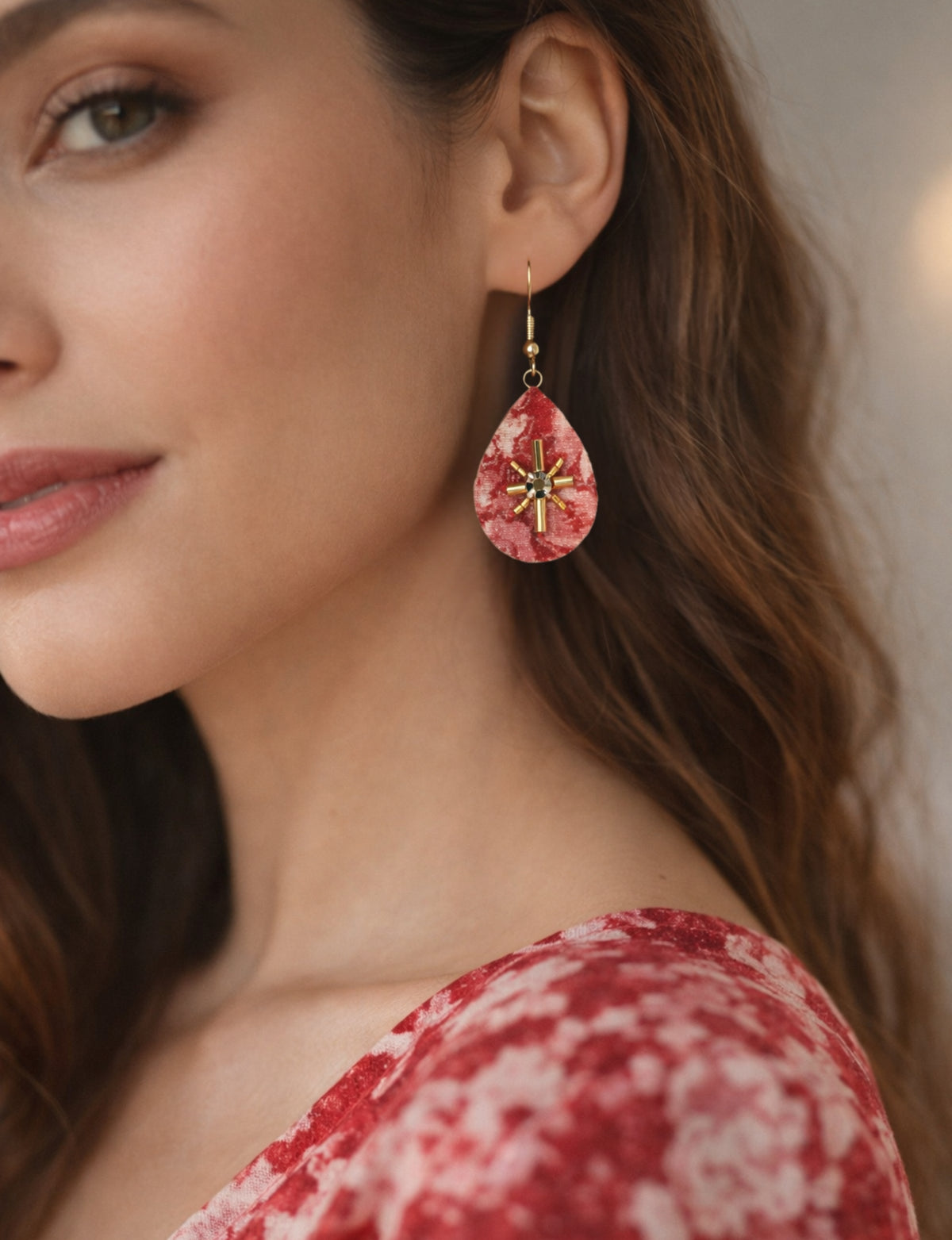 Red abstract teardrop earrings with gold bead and black center detail worn by model in close-up side view