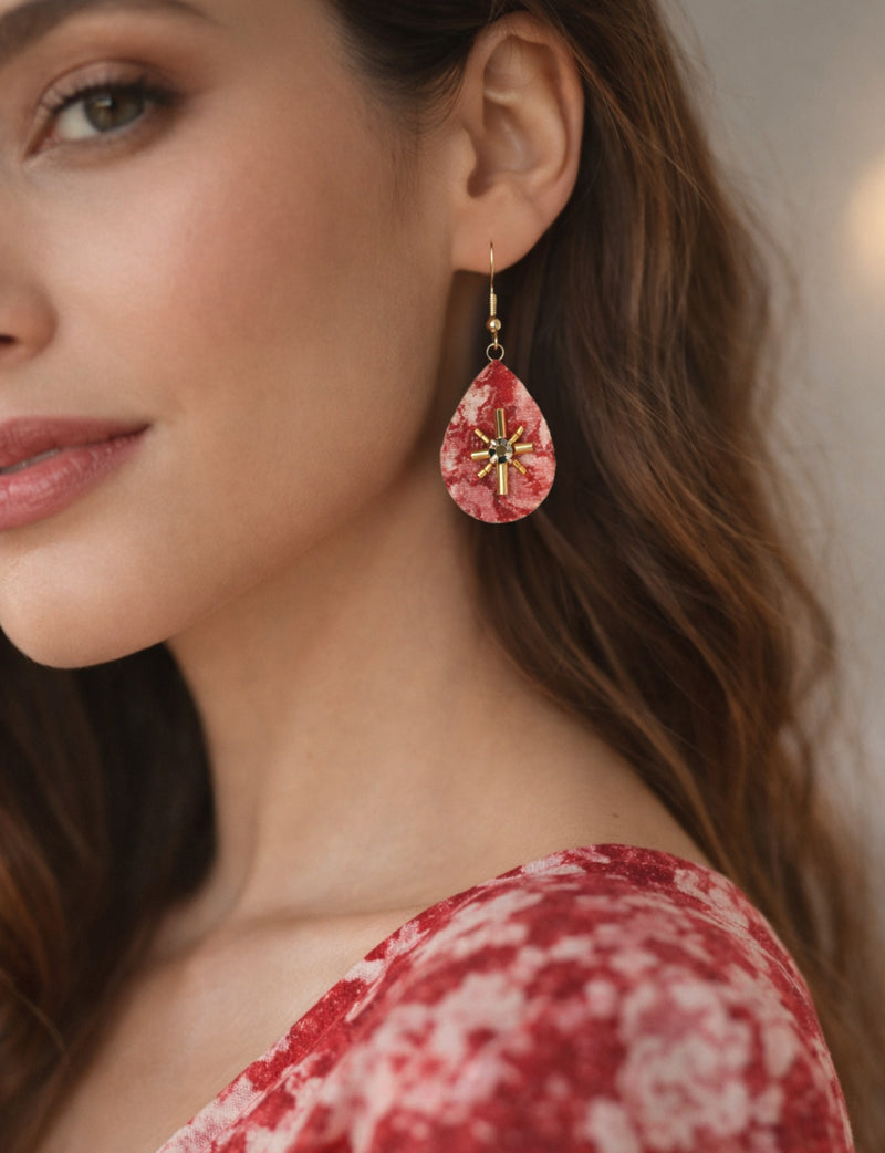 Red abstract teardrop earrings with gold bead and black center detail worn by model in close-up side view