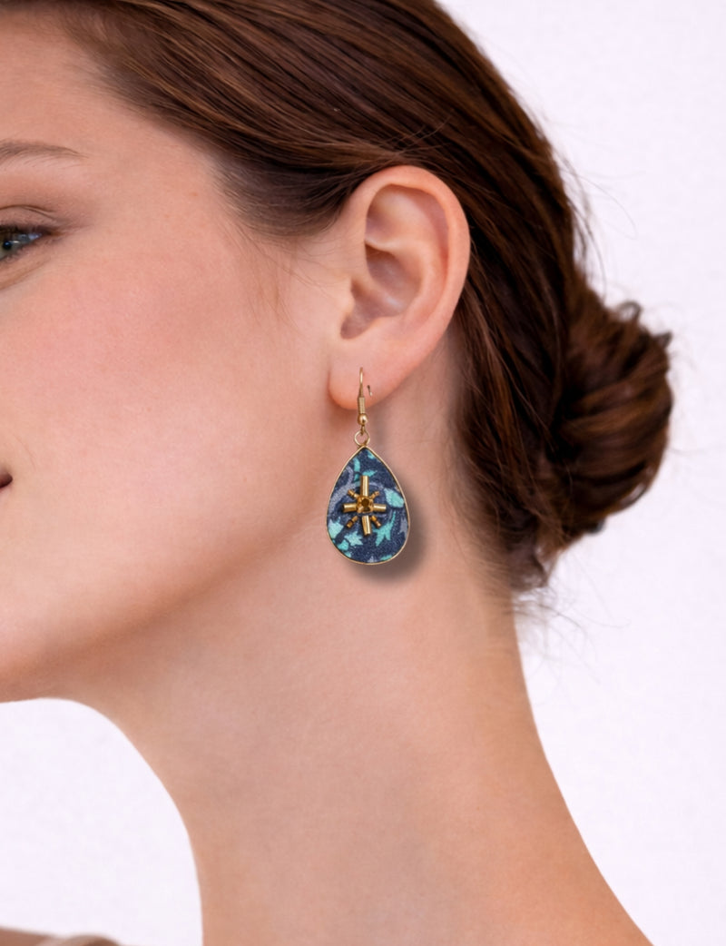 Woman wearing blue abstract teardrop earrings with gold-tone metal accents and hook closure, side view close-up