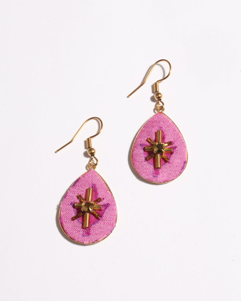 Pink teardrop earrings with gold-tone hooks and central gold bead and tube embellishments on fabric surface