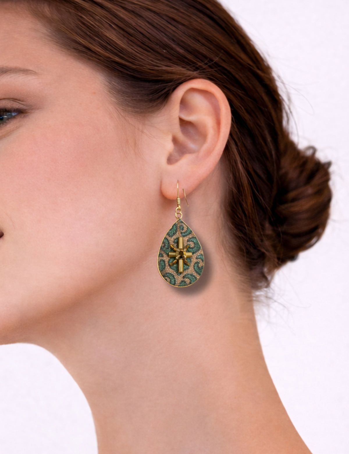 Woman wearing green teardrop earrings with gold-tone cross and micro swirl design, side view close-up